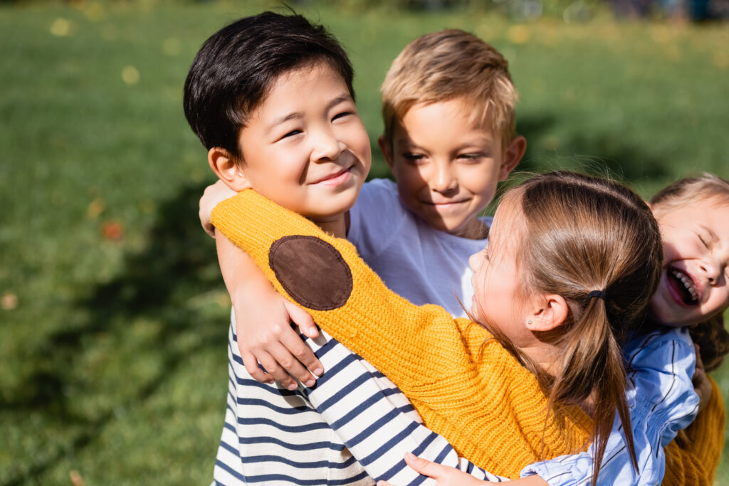 A group of children hugging and smiling outdoors, fostering empathy and friendship.