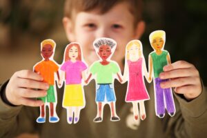 A young child proudly holding paper cutouts of diverse people, symbolizing inclusivity and empathy.