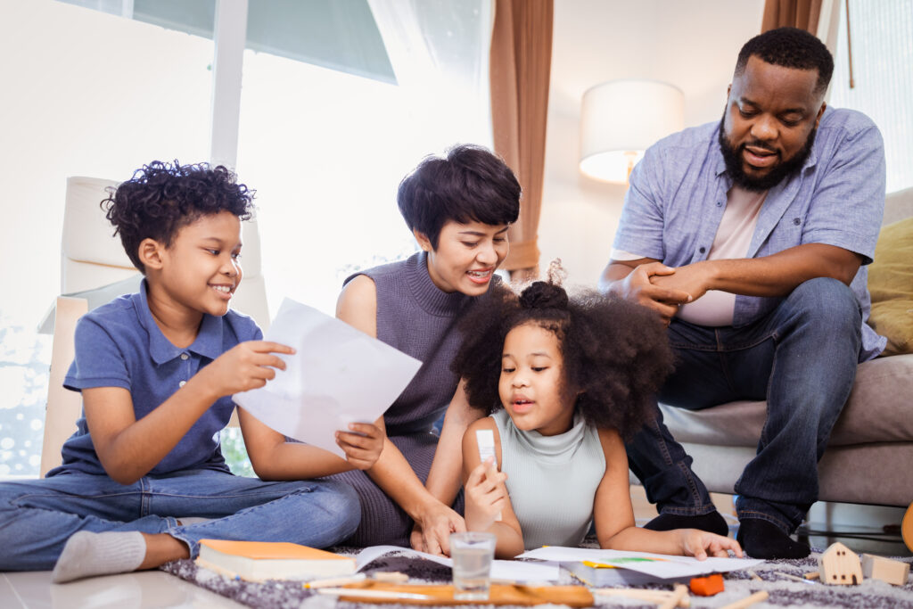 Happy family sitting on the floor, painting together while bonding in a cozy living room.