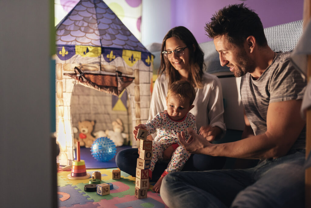 Parents enjoying playtime with their toddler son at home, building with wooden blocks.