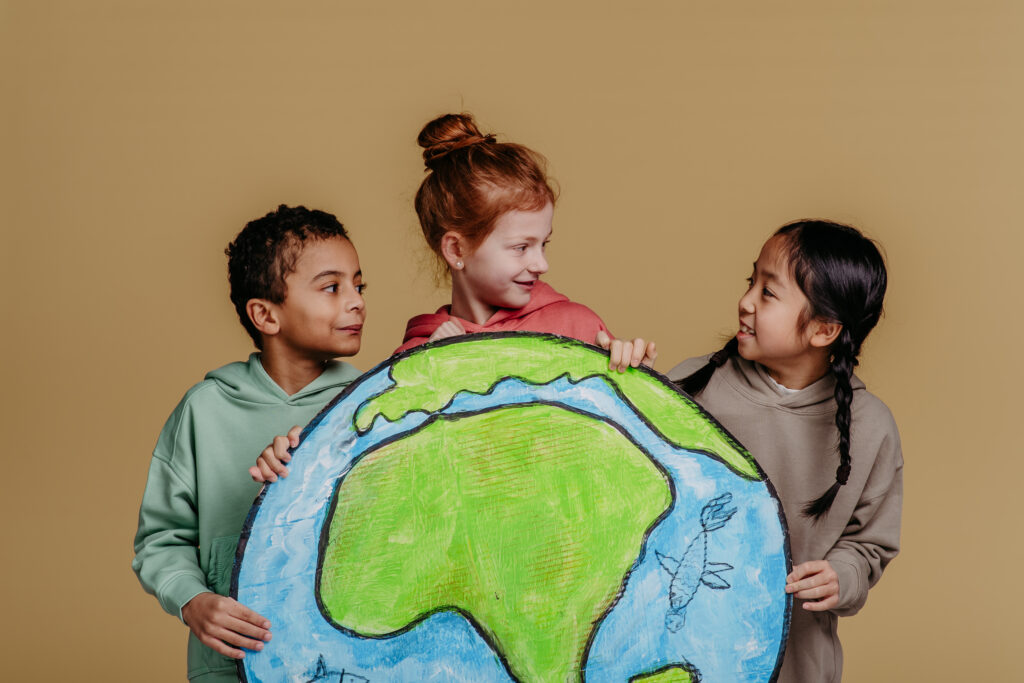Three children holding a globe: Three diverse children, standing together, smiling and holding a large hand-drawn model of Earth, showing their collaborative spirit and curiosity about the world.