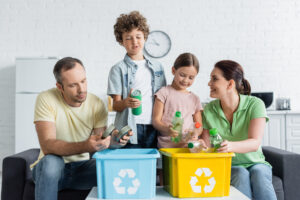 Family sorting recyclable materials into bins, teaching children about recycling cans and plastic bottles.