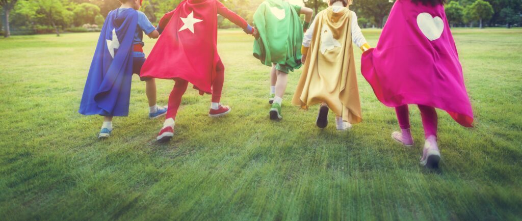 Children running together in colorful superhero capes, celebrating teamwork and empowerment.