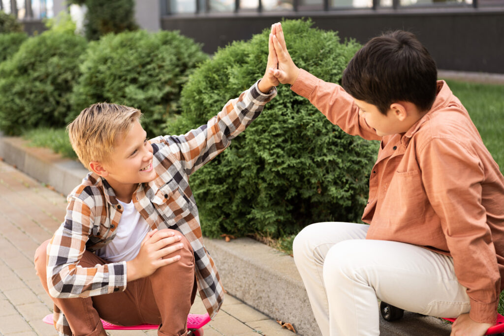 Two boys sitting outdoors, smiling and giving each other a high-five, reflecting friendship and collaboration
